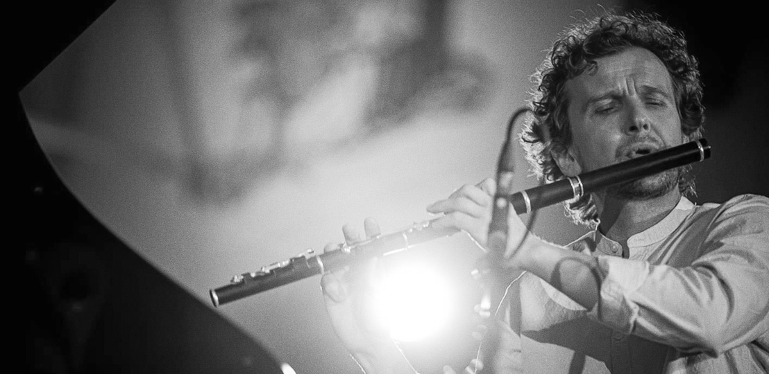 Michał Żak on stage during a performance, playing the wooden flute. The artist is focused on playing.